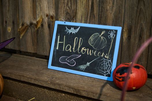A chalkboard halloween lettering on a wooden threshold and a small bright orange pumpkin. October 31. Porch or backyard decoration for Halloween