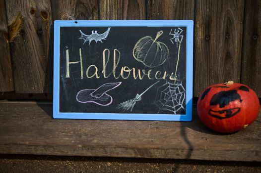 A blackboard with lettering Halloween and small pumpkin on the wooden doorstep. Halloween trick and treat