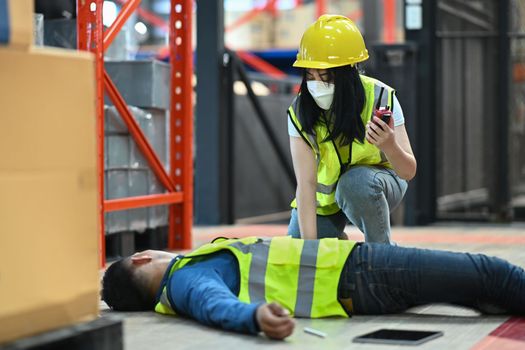 Female storehouse worker helping her coworker lying on the floor in warehouse. Safety first concept.