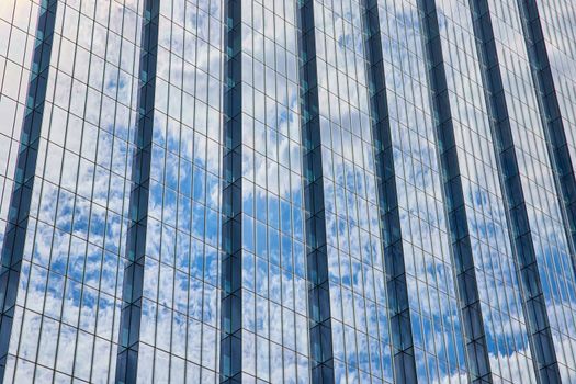 Image of Detail of huge glass skyscraper reflecting blue sky and clouds