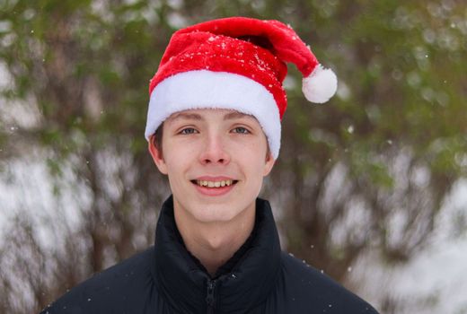 Close-up portrait of a 14-17 year old weighty boy wearing a Santa hat in snowy weather.