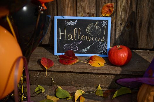 Close-up of a chalkboard with lettering Halloween, a pumpkin on the wooden doorstep with dry autumn fallen leaves