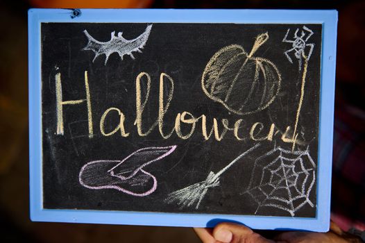 Close-up of a blackboard with lettering Halloween and drawn cobweb and wizard's hat with colorful chalks. October 31. Halloween trick and treat