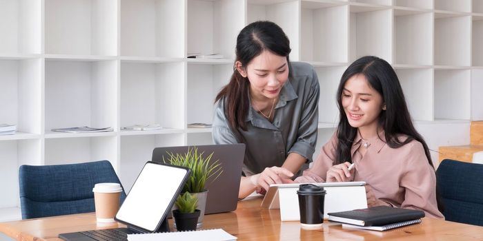 Two young Asian business woman talk, consult, discuss working with new startup project idea presentation analyze plan marketing and investment in the office...