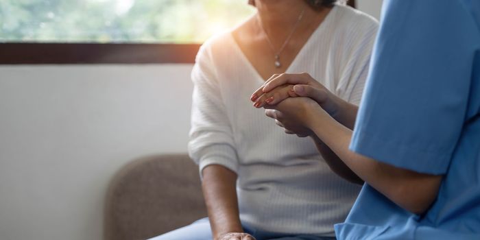 Happy patient is holding caregiver for a hand while spending time together. Elderly woman in nursing home and nurse...