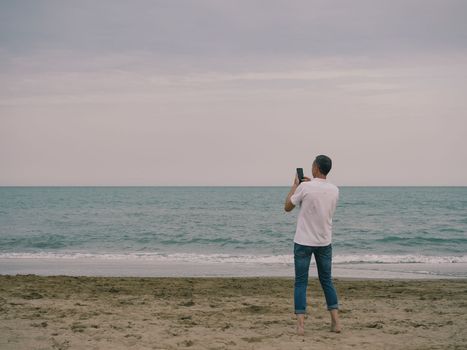 Young man taking picture photo of beach sunset holding a smartphone