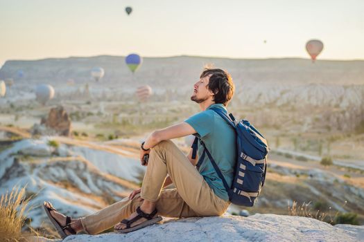 Tourist man looking at hot air balloons in Cappadocia, Turkey. Happy Travel in Turkey concept. Man on a mountain top enjoying wonderful view.
