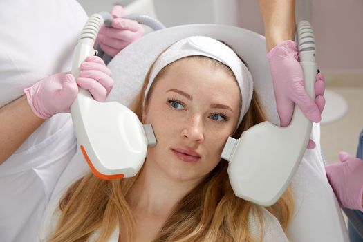 Conceptual beauty and cosmetology image of hands of several doctors holding laser equipment over female face. Cosmetology concept