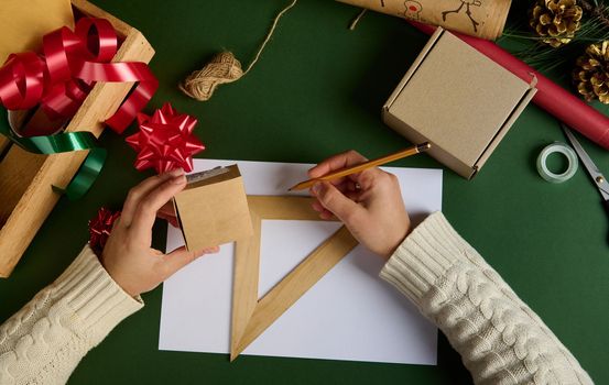 Top view woman's hands, hold cardboard box, calculates the amount of wrapping material for packing gifts for Christmas, Women's, Saint Valentine's Day or any other event using wooden ruler and pencil