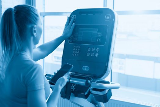 Sporty woman adjust settings on treadmill machine in gym