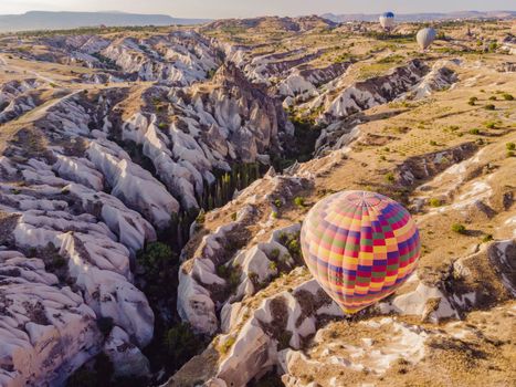 Colorful hot air balloons flying over at fairy chimneys valley in Nevsehir, Goreme, Cappadocia Turkey. Spectacular panoramic drone view of the underground city and ballooning tourism. High quality.