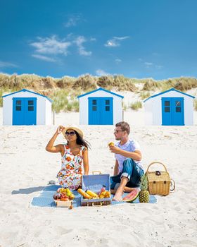 Picnic on the beach Texel Netherlands, couple having a picnic on the coast of Texel with white sand and a colorful withe and blue house in Holland