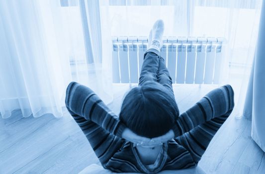 Woman laying on floor with feet raised up on radiator for warming