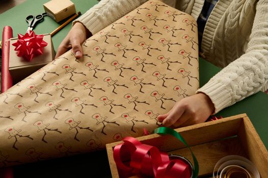 Selective focus on a wrapping gift paper with deer pattern in woman's hands, packing presents for Christmas or New Year. Boxing Day. New Year and Xmas preparations. Happy winter holidays. Diy presents