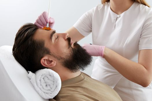 Cosmetologist applying a clay mask to male face. Spa treatment and face care in the beauty salon for men