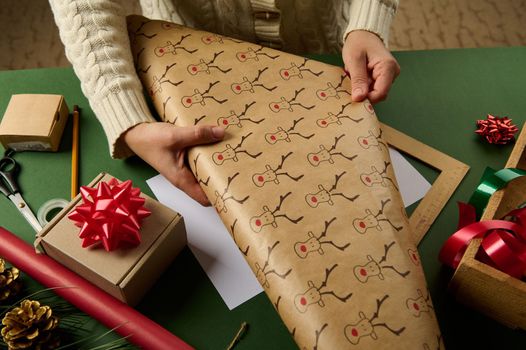 Details: woman's hands rolling out a wrapping gift paper with deer pattern, packing presents for Christmas or New Year. Boxing Day. New Year and Xmas preparations. Happy winter holidays. Diy presents