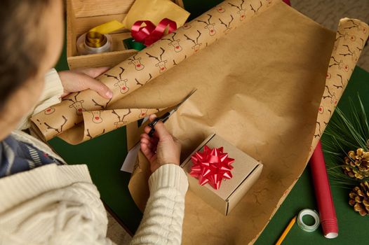 Overhead view of an unrecognizable woman, using scissors, cuts the decorative wrapping paper for packing gift for Christmas, New Year or other celebration event. Handsworkart. Boxing Day. Diy presents