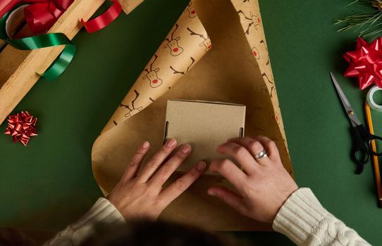 Top view woman's hands putting cardboard box on decorative wrapping paper with deer pattern. Packing presents. Boxing Day. Magical atmosphere of winter holidays. Christmas and New Year's preparations