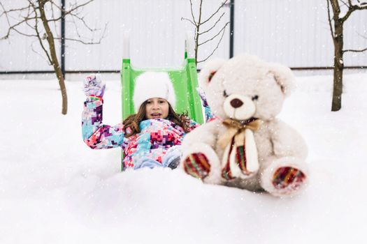 Cute toddler girl playing with teddy bear in winter park. Winter portrait of little caucasian child girl. Outdoor winter activities for kids.