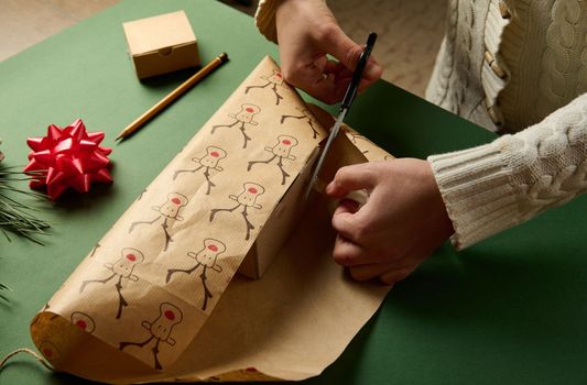 Top view woman packing a present for Christmas or New Year's events, using beautiful decorative wrapping paper with deer pattern, over a green background. Boxing Day. Xmas preparations. Copy ad space