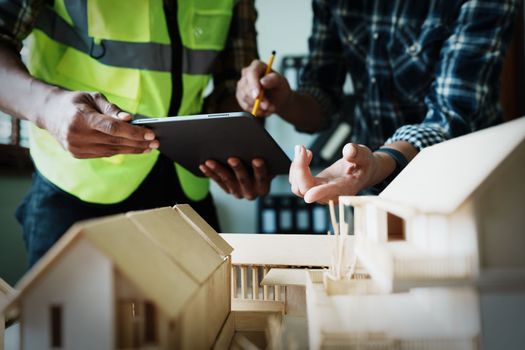 Engineers are consulting the team to design an architectural structure for clients with blueprints and building models to work at office.