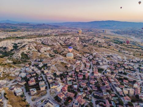 Colorful hot air balloons flying over at fairy chimneys valley in Nevsehir, Goreme, Cappadocia Turkey. Spectacular panoramic drone view of the underground city and ballooning tourism. High quality.