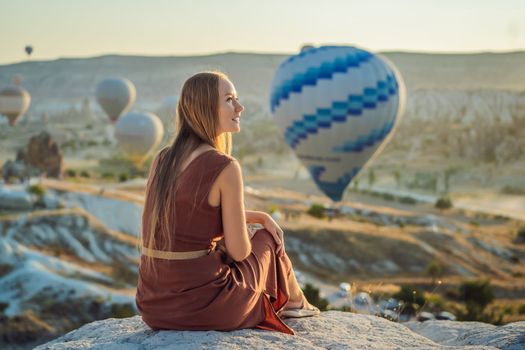 Tourist woman looking at hot air balloons in Cappadocia, Turkey. Happy Travel in Turkey concept. Woman on a mountain top enjoying wonderful view.