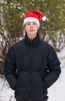 A boy of 14-17 years old in a black jacket and a red Santa hat keeps his hands in his pockets.