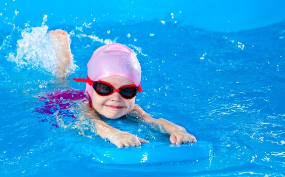 Preschool cute girl learning to swim in indoor pool with flutterboard