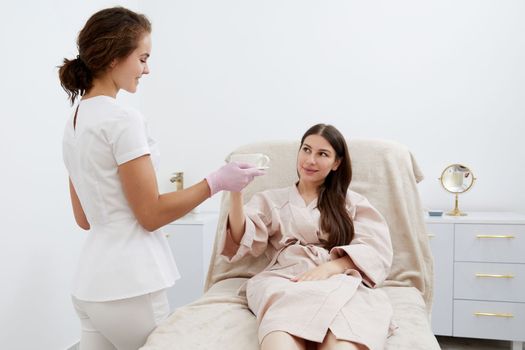 Beautician serving cup of coffee to her client after body treatment in beauty salon. Relaxing with beverages on cosmetic bed. Beauty , pleasure concept