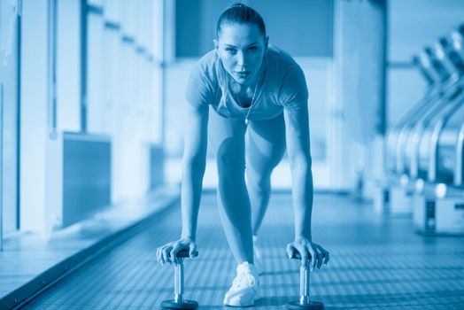 Physically fit woman at the gym lifting dumbbells to strengthen her arms and biceps. Muscular woman sitting on exercise mat looking at her arms.