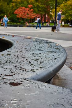 Image of Cement concrete curved seating with patches of water drops and tourists soft in background