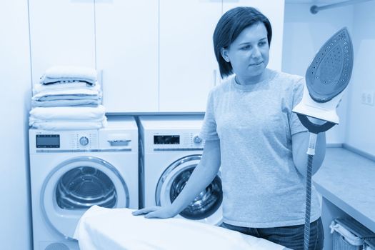 Woman ironing white shirt on board in laundry room with washing machine