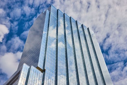 Image of Top of large glass skyscraper reflecting blue sky