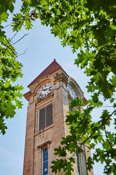 Image of Green leaves frame limestone clock tower on college campus