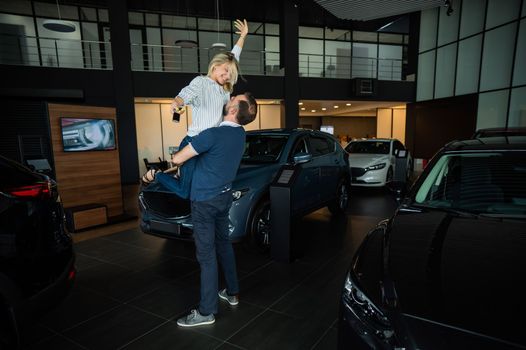 Happy caucasian couple hugging while buying a new car in a car dealership