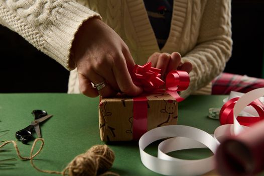 Woman's hands decorate a Christmas gift with tied bow. Packing presents for New Year or any other celebration event. December 25th. Boxing Day.