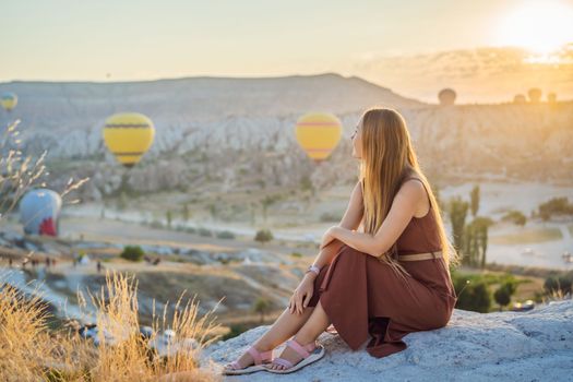 Tourist woman looking at hot air balloons in Cappadocia, Turkey. Happy Travel in Turkey concept. Woman on a mountain top enjoying wonderful view.