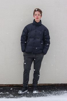 Cute teenage boy at full height in front of a wall in snowy weather.