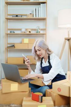 Starting small business entrepreneur of independent Asian woman smiling using computer laptop with cheerful success of online marketing package box items and SME delivery concept.