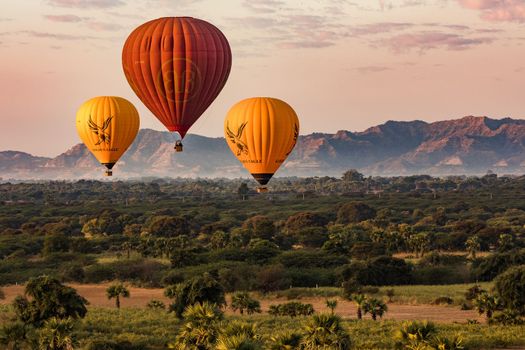 Aerial view from a hot air balloon with fields, palm trees and mountains over the cultural complex of Bagan in Myanmar