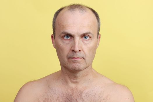 A man 45-55 years old without clothes with a hairy chest on a yellow background.