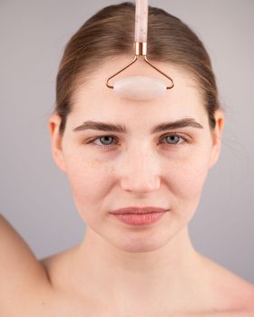 Close-up portrait of a woman uses a quartz roller massager to smooth wrinkles on her forehead