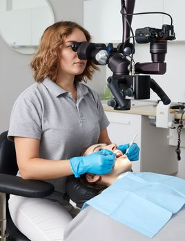 Female dentist with dental tools and microscope treating patient teeth at dental clinic office. Medicine, dentistry and health care concept. Dental equipment