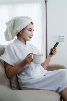 Woman with facial mask using phone at home. Skin care, face treatment, spa, cosmetology and natural beauty concept