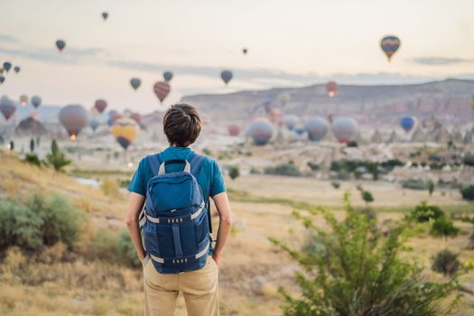 Tourist man looking at hot air balloons in Cappadocia, Turkey. Happy Travel in Turkey concept. Man on a mountain top enjoying wonderful view.