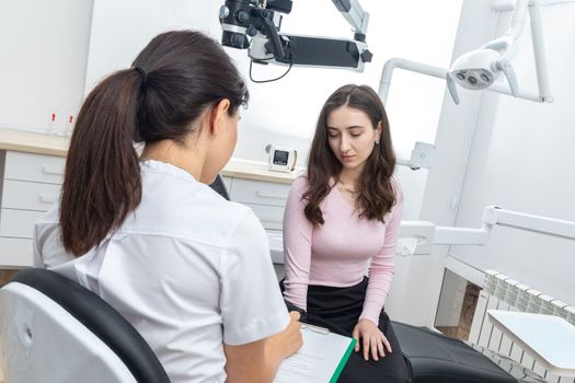 Female dentist filling in papers while talking to a patient in dental office