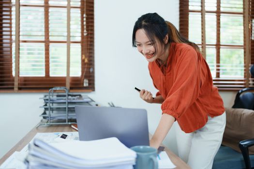 Portrait of a woman business owner showing a happy smiling face as he has successfully invested her business using computers and financial budget documents at work.