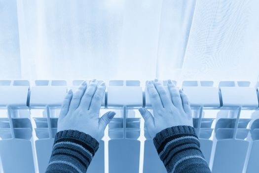 Girl warms up the frozen hands above hot radiator, close up