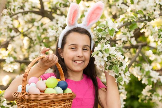 A little girl with pink rabbit ears. painted eggs in the park. Easter. Copy space